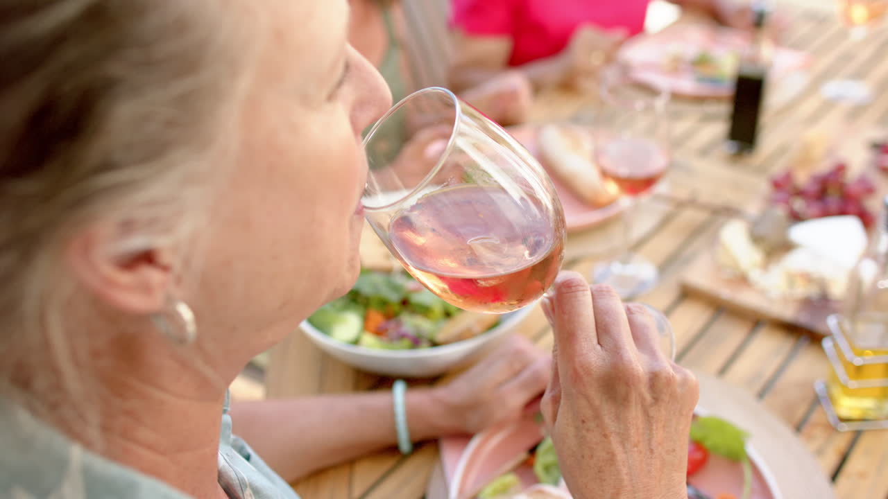 Femme âgée métisse savourant un verre de vin à une table à manger en extérieur