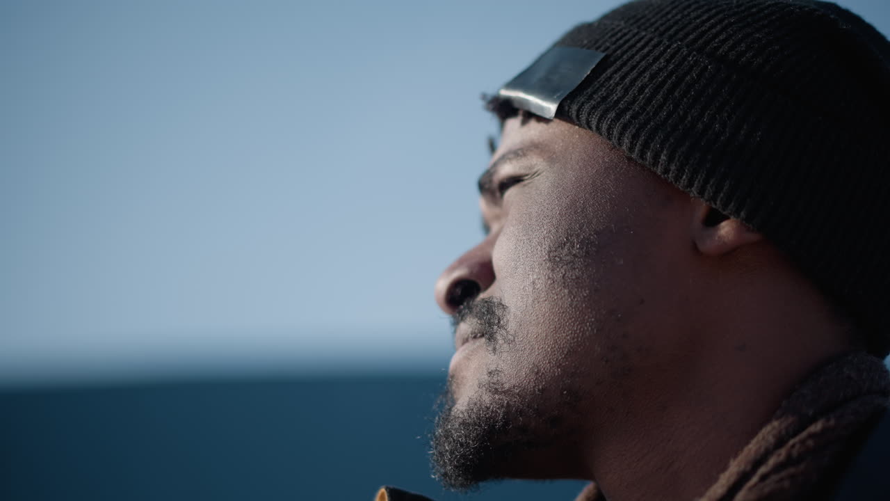 close up aerial view of city dweller in winter coat beanie and gloves sipping hot beverage through straw while lifting head to survey snowy urban street with camera strap and soft daylight glow