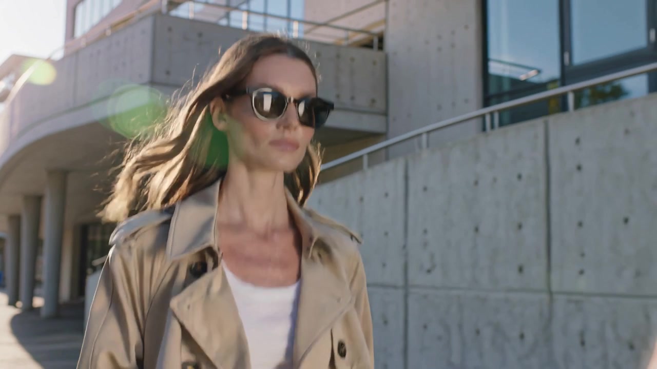 Donna elegante in trench e occhiali da sole che cammina all'aperto