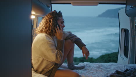 happy camp tourist calling smartphone in camper van at gloomy sea coast close up