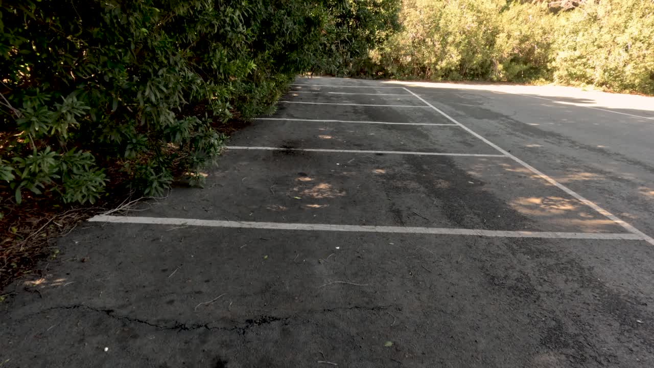 A person walks along a sidewalk with sunlight and shadows mixing on the ground. The surface has marks and patches, creating an interesting view in the afternoon