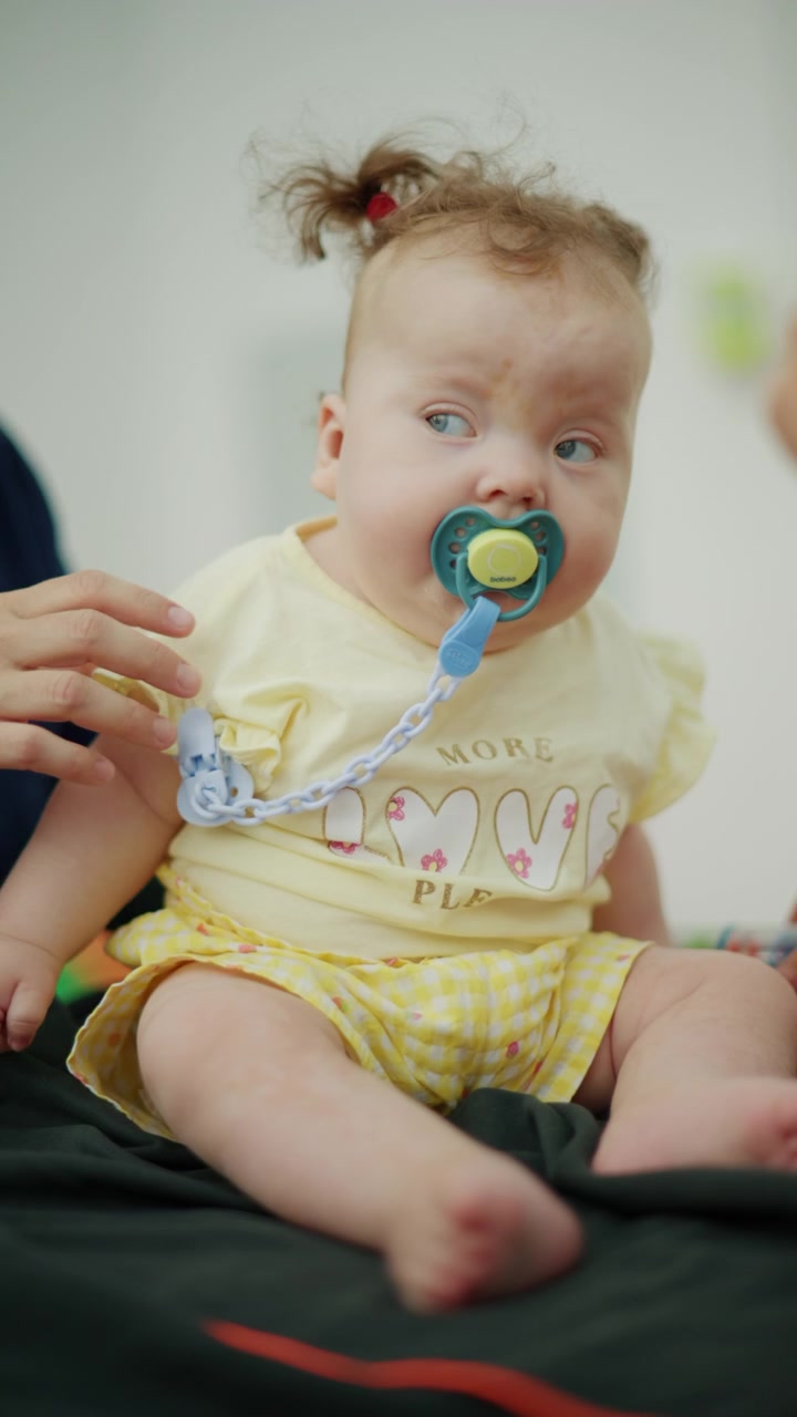Baby sitting on a parent's lap, wearing a yellow shirt and holding a pacifier, showing innocence