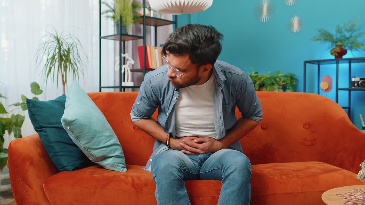 Arabian man sits on sofa feeling sudden strong abdominal stomach ache gastritis problem diarrhea