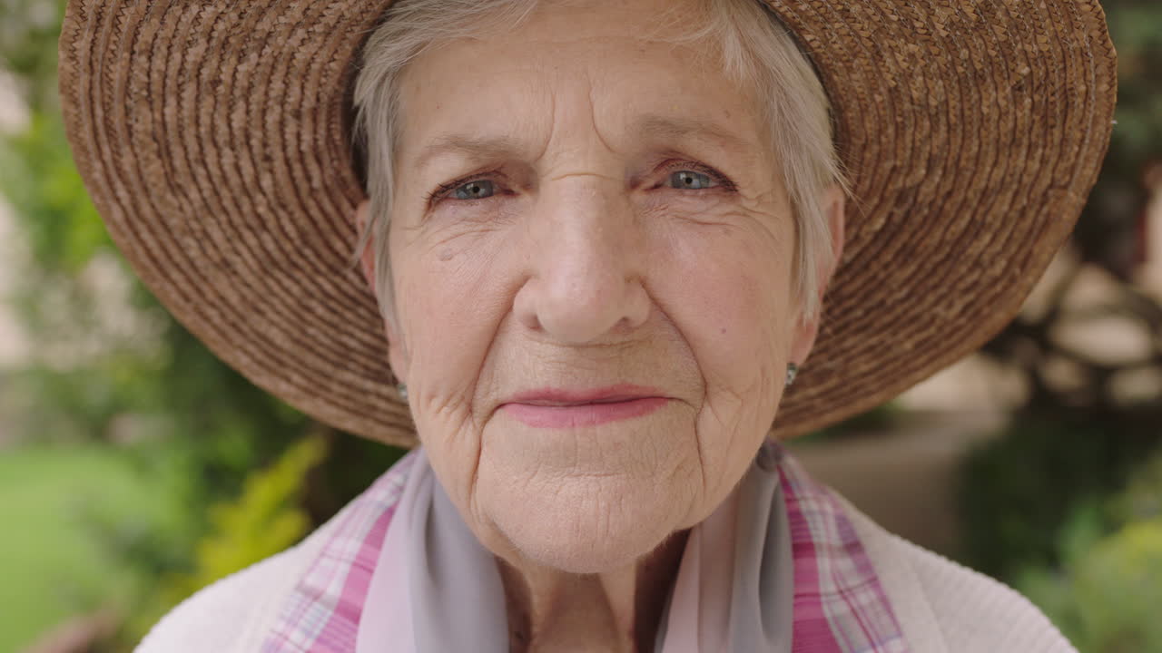 retrato en primer plano de una anciana mirando a la cámara sonriendo feliz con un sombrero disfrutando del jardín soleado al aire libre