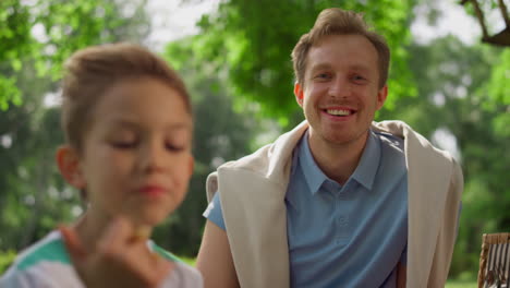 winking happy man laughing on camera close up. father seat with son on picnic.