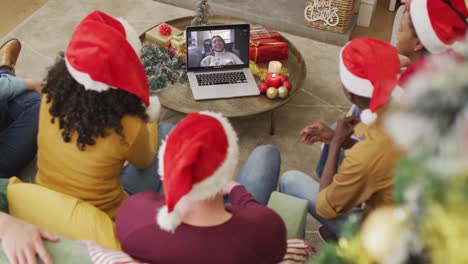 Eine-Vielfältige-Familie-Mit-Weihnachtsmützen-Nutzt-Laptop-Für-Einen-Weihnachtsvideoanruf-Mit-Einer-Glücklichen-Frau-Auf-Dem-Bildschirm