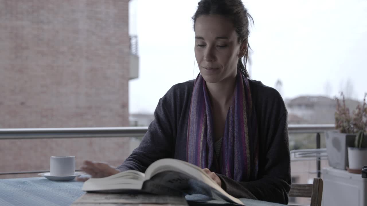 Eftertænksom kvinde, der læser en bog på en balkon