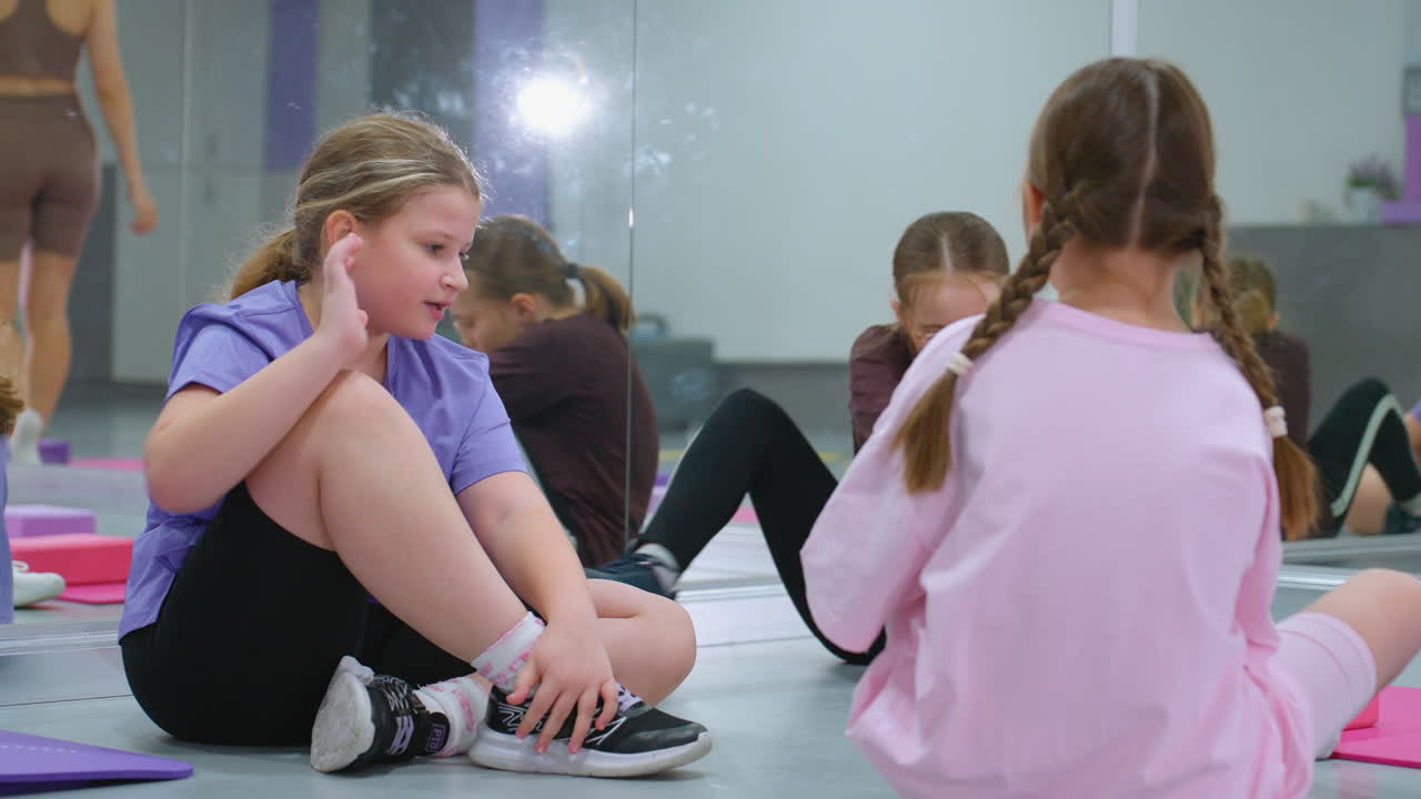 체육관에 앉아있는 아이들이 운동 후에 휴식을 취하고, 거울이 반사되는 체육관 감독이 배경에 있습니다. 보라색 옷을 입은 한 아이는 다른 아이들이 는 동안 도망치려고 준비하고 있습니다.