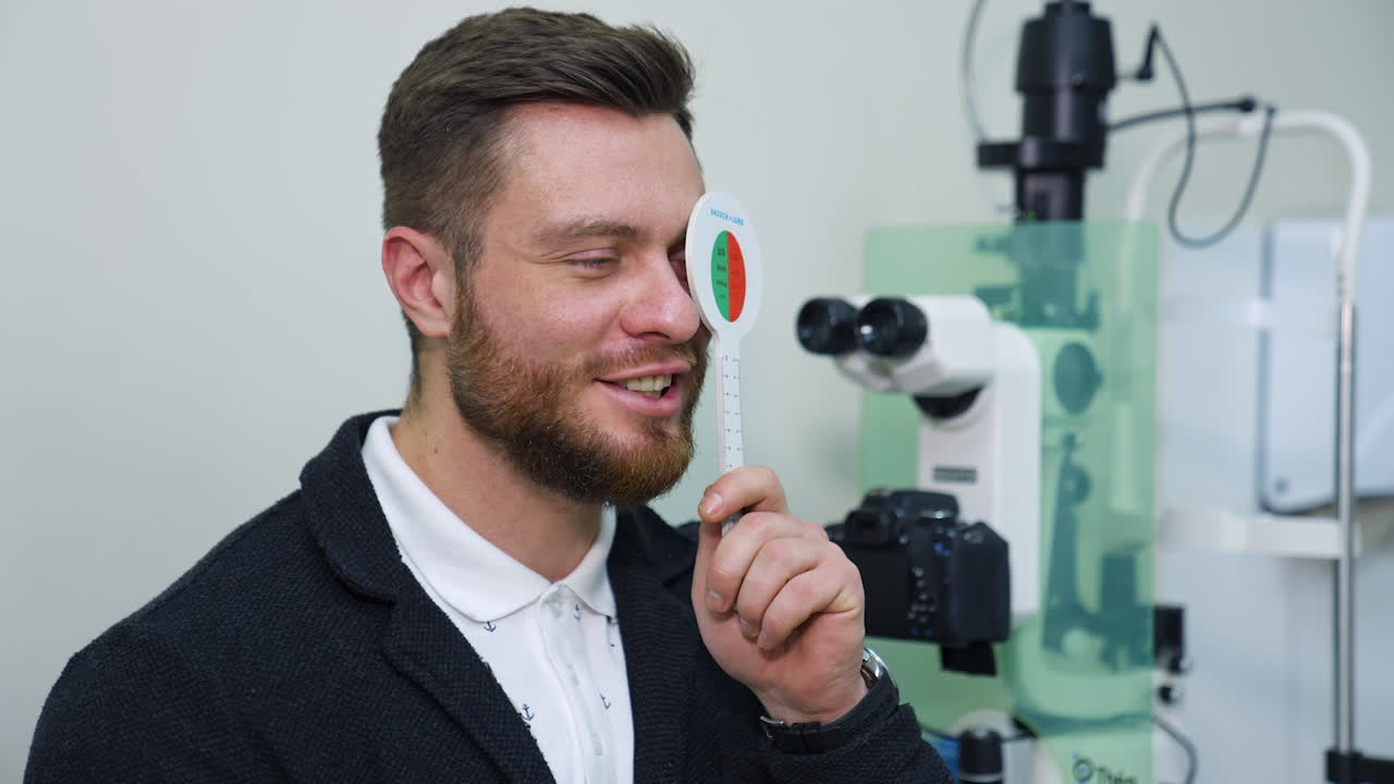 Young man at ophthalmologist's. Checking eyesight in clinic. Patient closing one eye to test his vision. Optical concept.