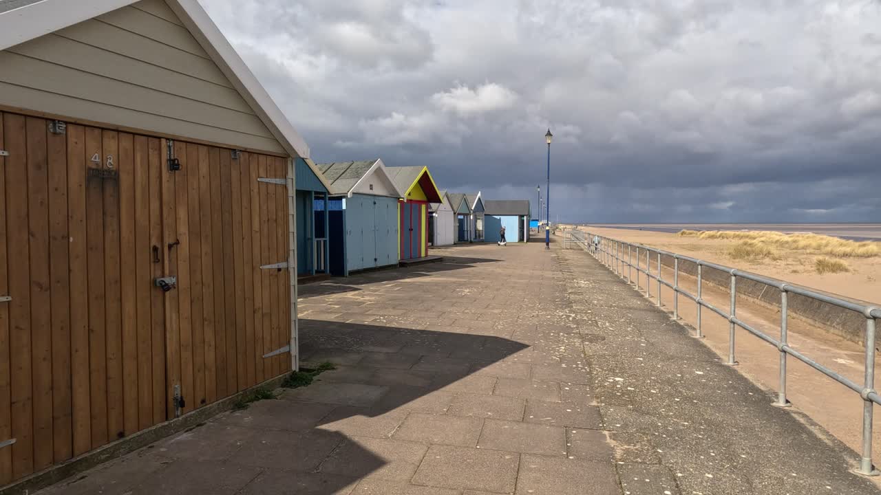 Colorful beach huts stood in a line along the seafront with sandy beach and moody grey sky&rsquo;s