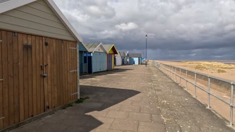 colorful beach huts stood in a line along the seafront with sandy beach and moody grey sky’s