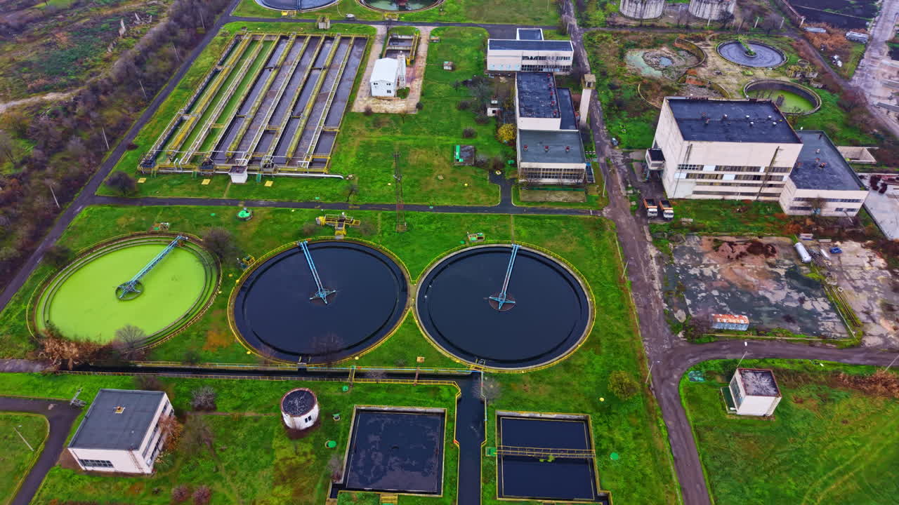 Wastewater treatment facility shows multiple processing tanks and surrounding green areas in an industrial setting