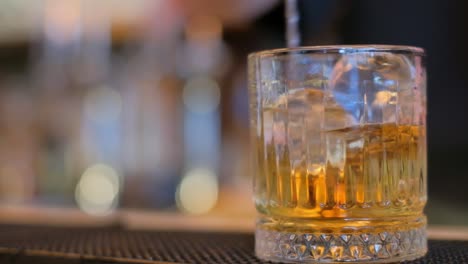 A visually appealing cocktail served over ice in a stylish glass, set against a blurred bar backdrop
