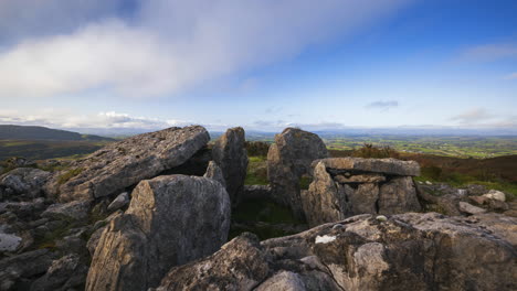 timelapse of rural nature landscape with ruins of prehistoric passage tomb stone blocks in the foreground during sunny cloudy day viewed from carrowkeel in county sligo in ireland