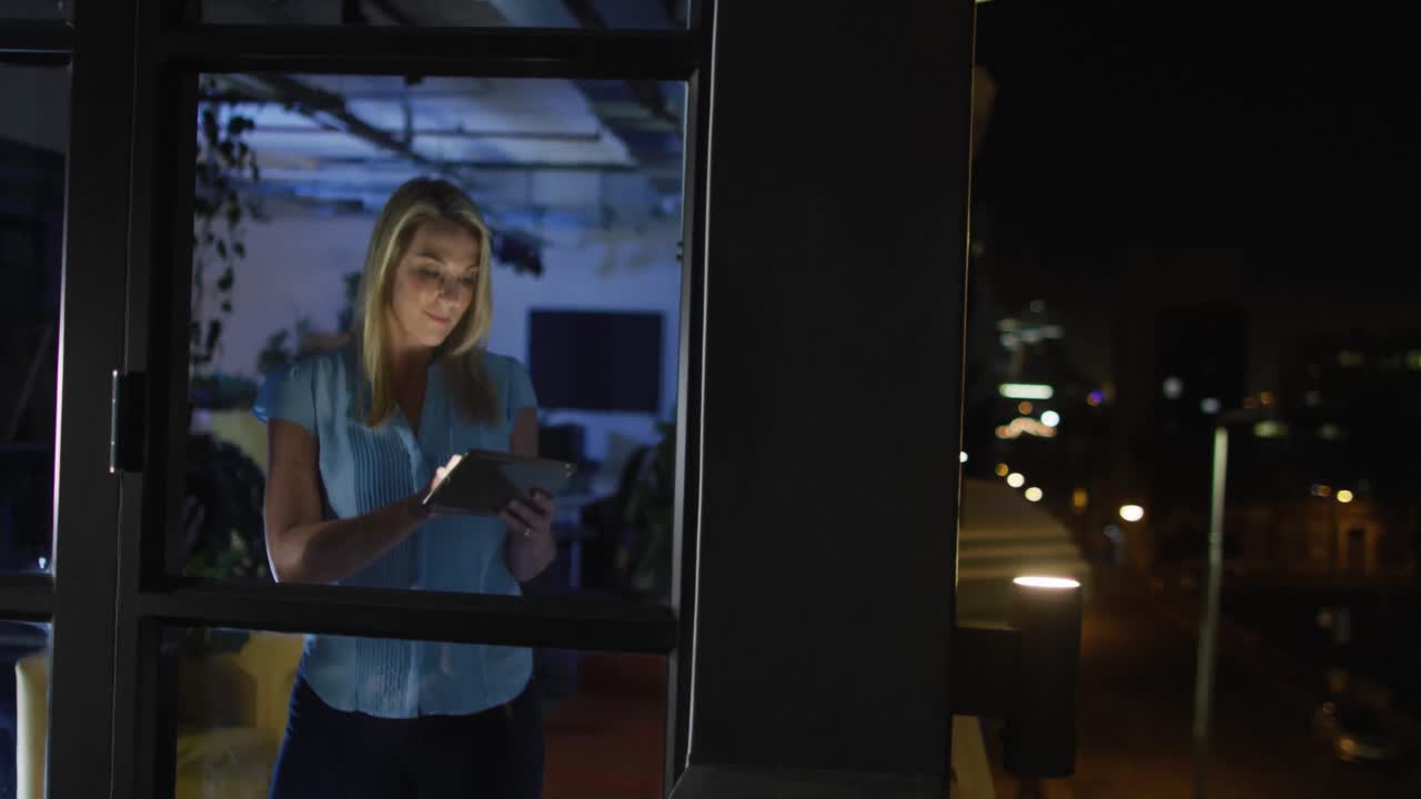 Video di una donna caucasica con tablet che lavora fino a tardi in ufficio.