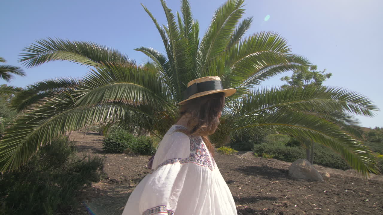 молодая женщина улыбается и протягивает руки к солнцу, стоя под пальмой в красивом летнем пейзаже.