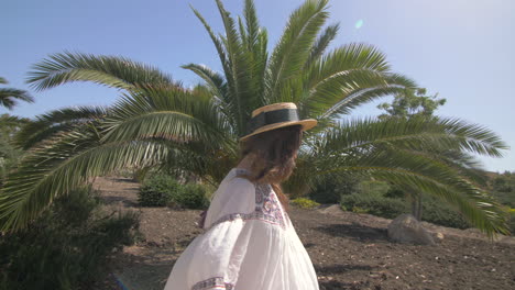 una mujer joven sonríe y extiende los brazos hacia el sol, de pie bajo una palmera en un hermoso paisaje de verano.
