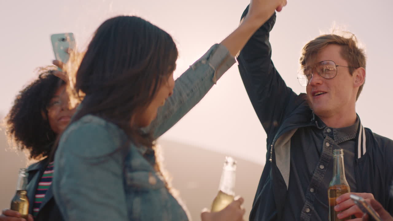 다민족 친구 그룹이 어울리고 있습니다. 젊은 아시아 여성이 춤을 추고 있습니다. 해가 지면 옥상 파티를 즐기고 있습니다. 주말 축하를 즐기고 있습니다.