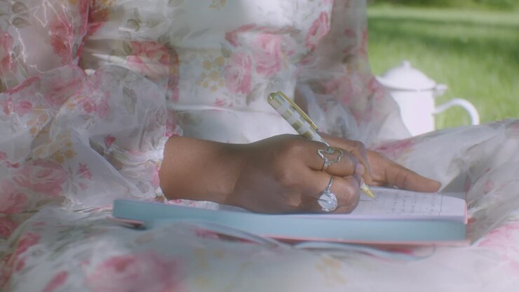 Black woman in white floral dress in park writes in her diary, close up
