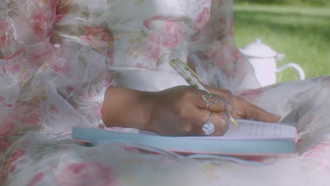 black woman in white floral dress in park writes in her diary, close up