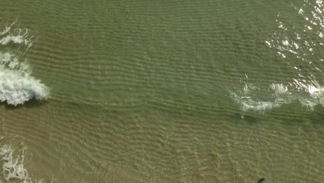 Toma-Panorámica-De-Inclinación-Aérea-De-Las-Claras-Olas-Del-Océano-Rompiendo-Lentamente-En-La-Playa