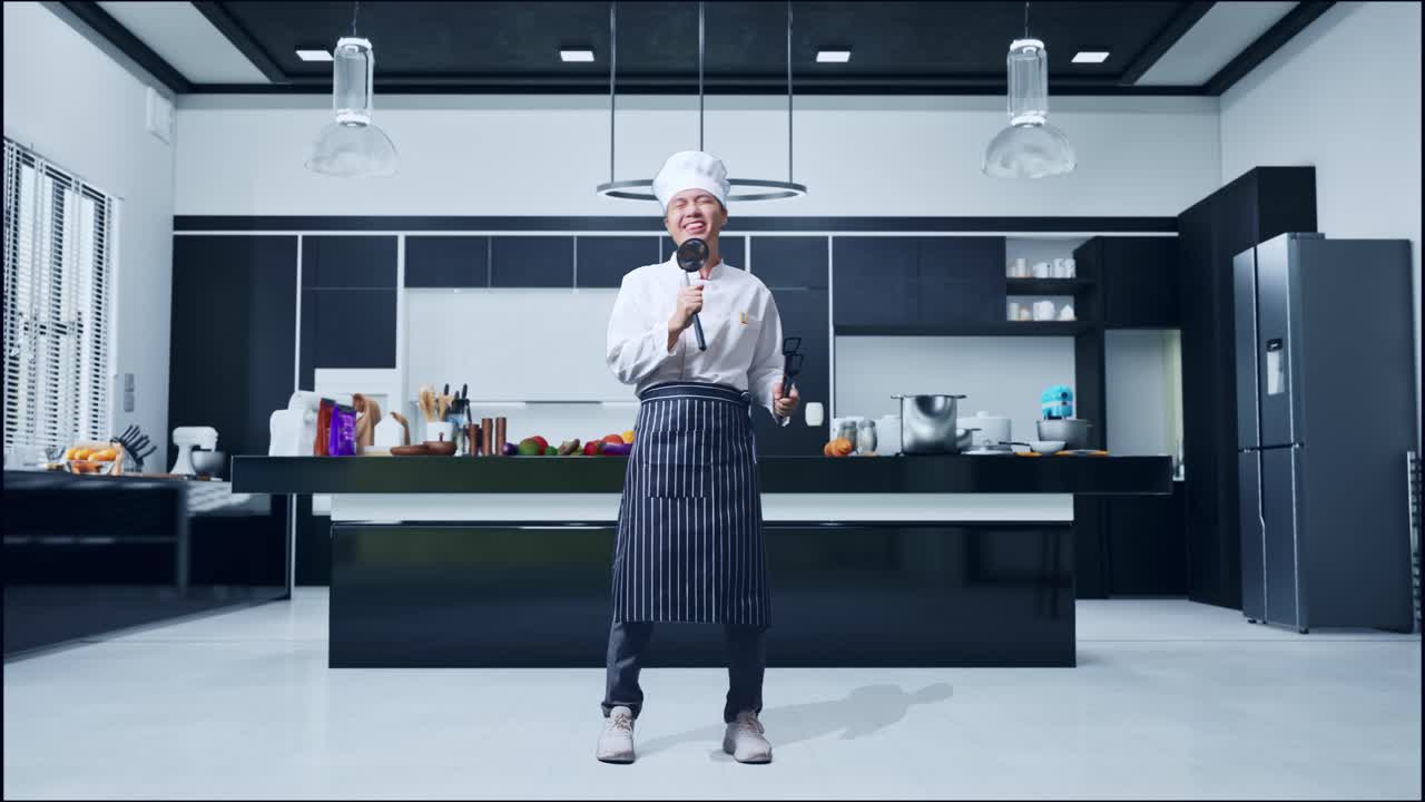 cuerpo lleno de cocinero hombre asiático sosteniendo pinzas y cuchara y cantando mientras está de pie en la cocina de casa