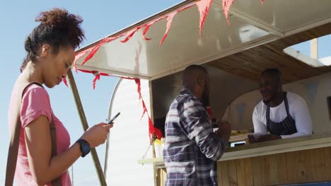 smiling mixed race woman using smartphone waiting in queue to be served at food truck