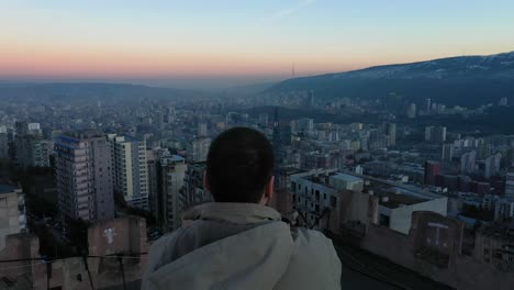 vista trasera de un hombre admirando el glorioso amanecer de la ciudad desde un tejado, inclinado hacia arriba