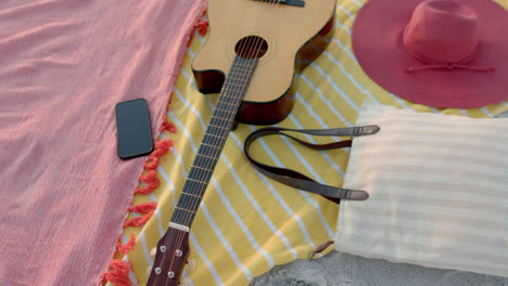 una guitarra está al lado de un sombrero y un teléfono en una manta de playa