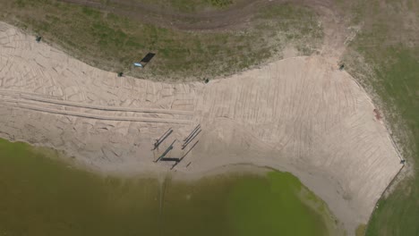 Blick-Von-Oben-Auf-Einen-Angelegten-Erholungssee-In-Den-Niederlanden,-Der-Den-Strand-Und-Die-Grünen-Felder-Rund-Um-Das-Grüne,-üppige-Wasser-Zeigt