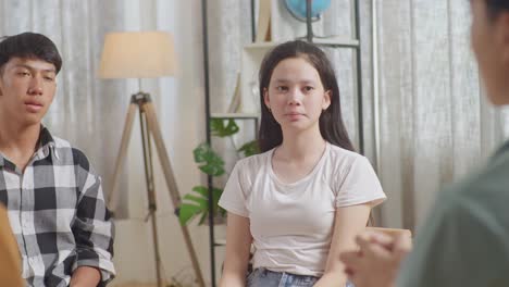아시안 십대 그룹이 집에서 앉아서 토론하고 있습니다. 회색 셔츠를 입은 소년이 동기를 부여하는 셔츠 셔츠와 소녀, 코치, 계획 프로젝트의 근접 뒷면