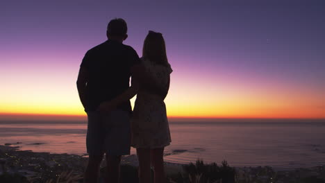 Couple-standing--on-a-beach-by-the-sea-at-sunset,-silhouette