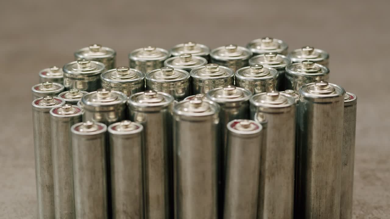 Silver batteries AA and AAA on black background close-up. Double-A battery is a standard size single cell cylindrical dry battery. Batteries are common in portable electronic devices. An AA battery is composed of a single electrochemical cell that may be either a primary battery or a rechargeable ba