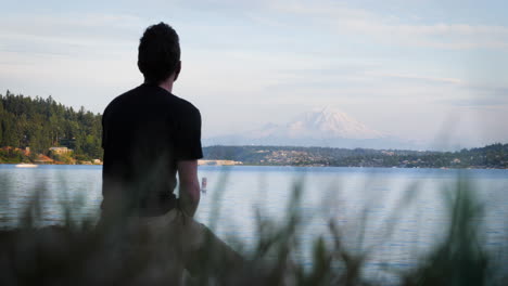 static shot of young man sitting at seward park looking out at mt