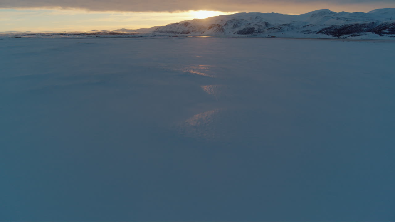 Sunset over snow covered mountains in Iceland during winter drone tilt up shot
