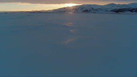 sunset over snow covered mountains in iceland during winter drone tilt up shot