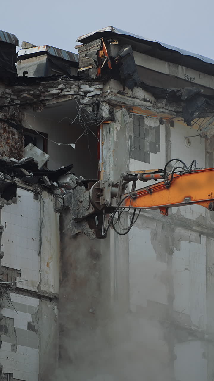 Hydraulic crasher of an excavator machine demolishing the house. High building wrecked by an earthquake being destroyed by a special machinery. Dust spreads all over the place. Vertical video