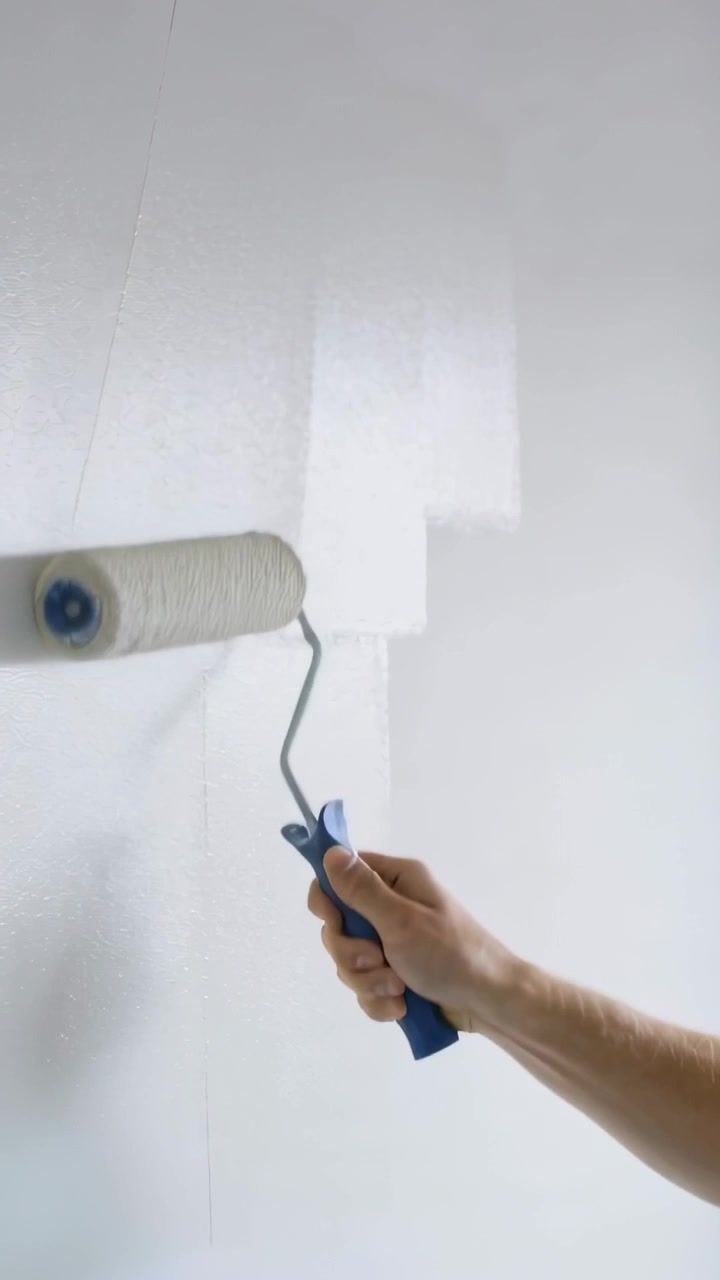 Video verticale: Uomo che dipinge con il braccio scoperto, muovendo un rullo blu a contatto con la parete per uniformare la pittura