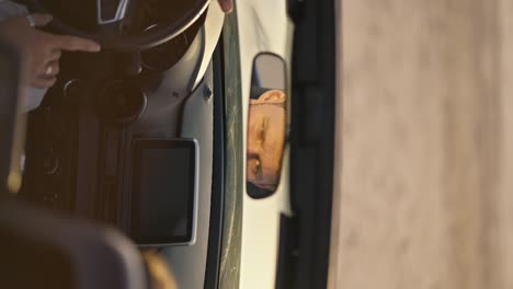 vertical video: a man thoughtfully looks into the car mirror, putting his finger on the steering wheel of the car