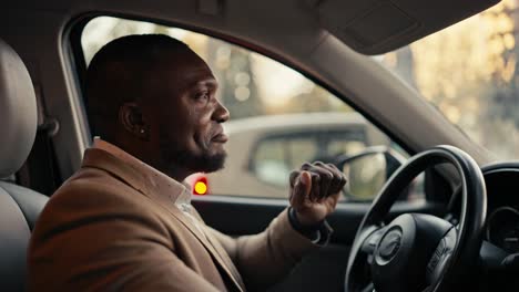 Happy-and-cheerful-man-Businessman-with-Black-skin-and-a-beard-in-a-brown-jacket-dances-while-sitting-in-the-cabin-of-a-modern-car-during-his-business-trip-in-the-city