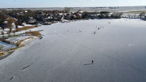 toma de drones de personas patinando sobre hielo en un lago congelado en los países bajos