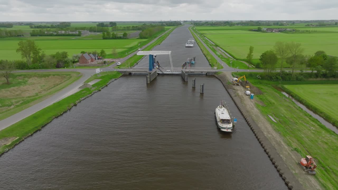 Oblique view of a canal worksite with service vehicles and a moored motor barge near a bascule bridge