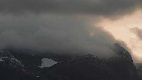 Nubes-Tormentosas-Iluminadas-Por-La-Puesta-De-Sol-Giran-Sobre-Las-Montañas-Nevadas-En-El-Vídeo-Timelapse