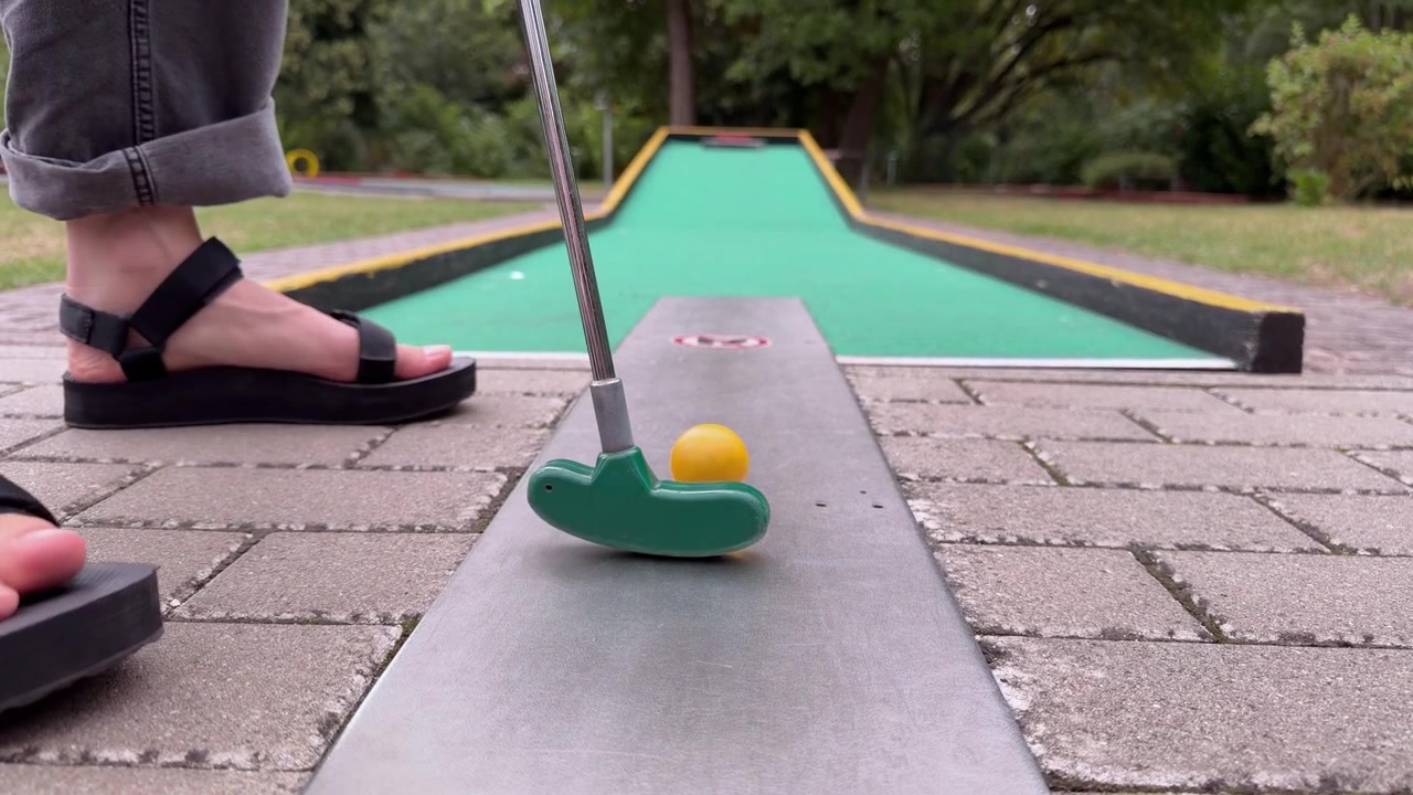 Person placerar gul boll och förbereder sig för att putta på en utomhus minigolfbana.