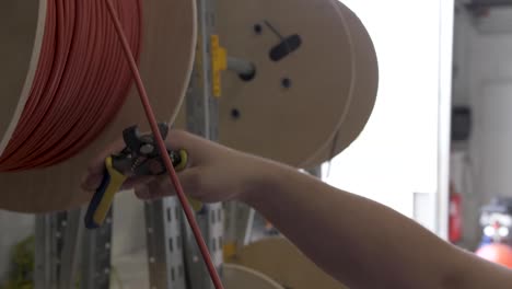 Corte-De-Cable-Rojo-Eléctrico-De-Un-Carrete-Utilizado-Para-La-Instalación-De-Paneles-Solares-Con-Una-Herramienta-De-Corte,-Tiro-De-Cierre-En-Cámara-Lenta