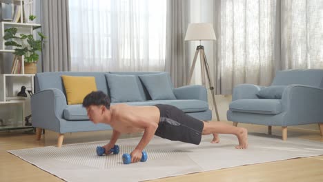 full body of asian teenager boy doing push ups with dumbbells on mat during the shirtless workout at home