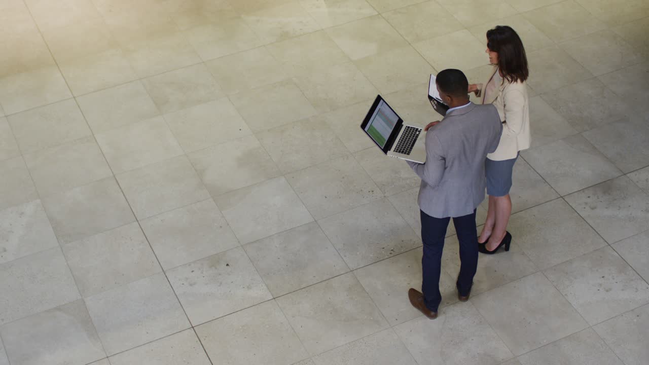 Diversos empresarios y empresarias hablando y usando un portátil en el vestíbulo de una oficina moderna