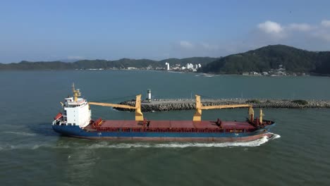 Aerial-View-Of-Barge-Sailing-Next-To-Farol-da-Barra-And-Seawall-To-Itajai-Acu-River-In-Brazil