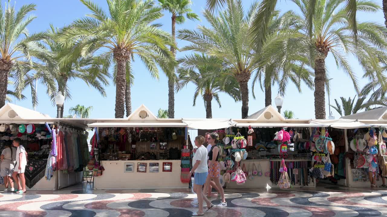 During the summer in Spain, tourists explore a street market situated on Alicante's famous landmark, La Explanada.