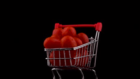 macro disparo de un carrito de supermercado lleno de tomates de uva roja amontonados con gotas de agua. girando en la mesa giratoria. aislado en el fondo negro. primer plano.